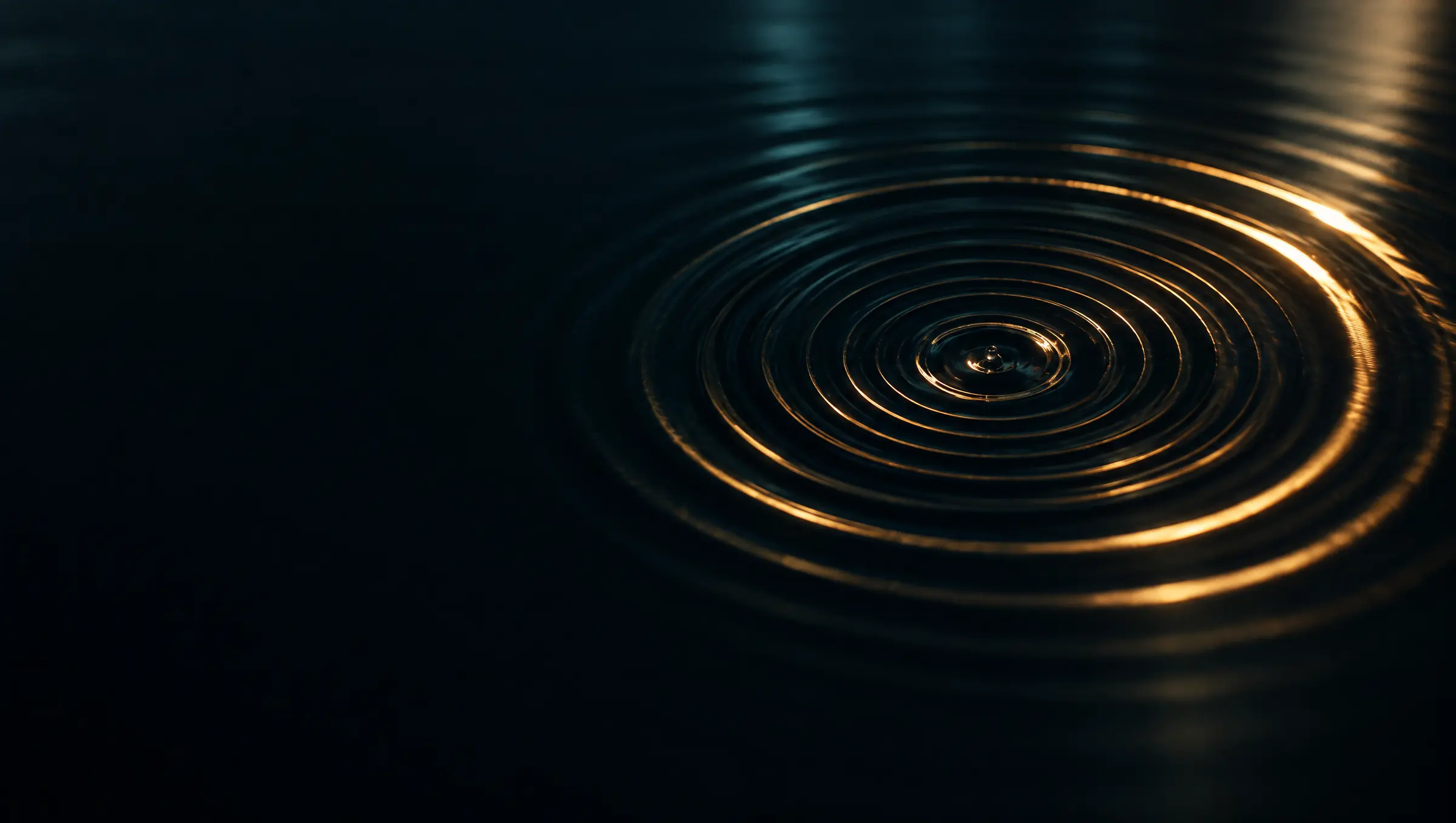 Gold rings of light spreading across dark, still water from a single drop.
